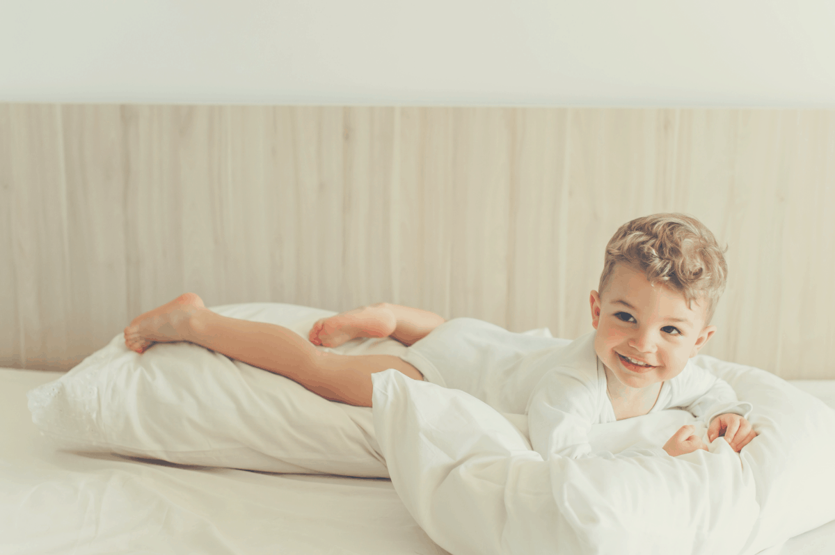smiling toddler boy playing with pillows in bed