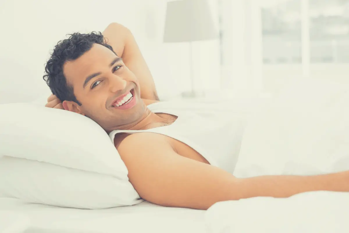 man smiling while lying on a pillow in bed