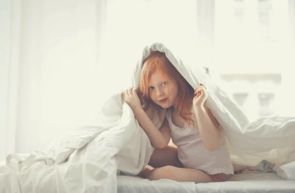 adorable girl on a bed wrapped in white comforter