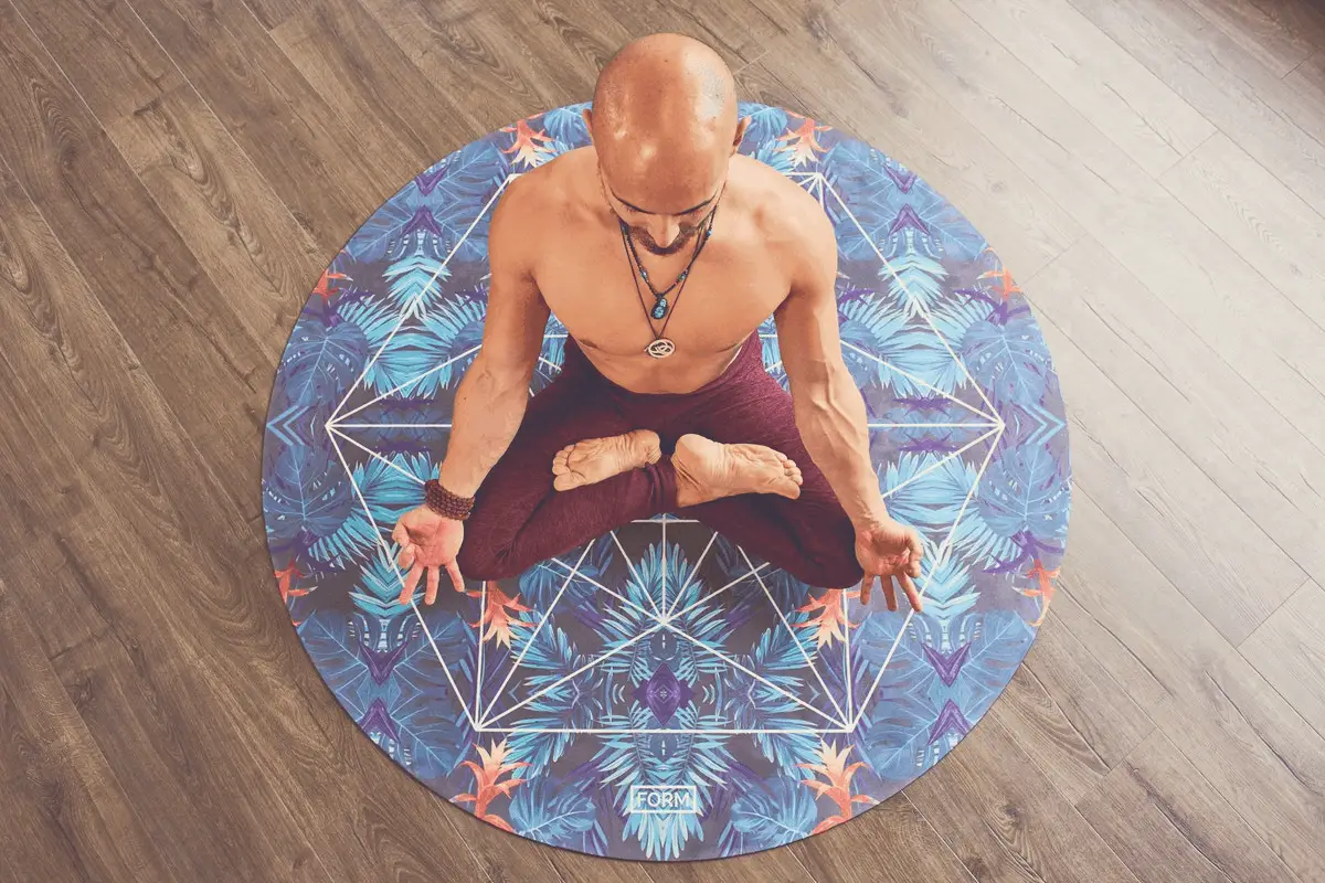 bare-chested man meditating on a hardwood floor