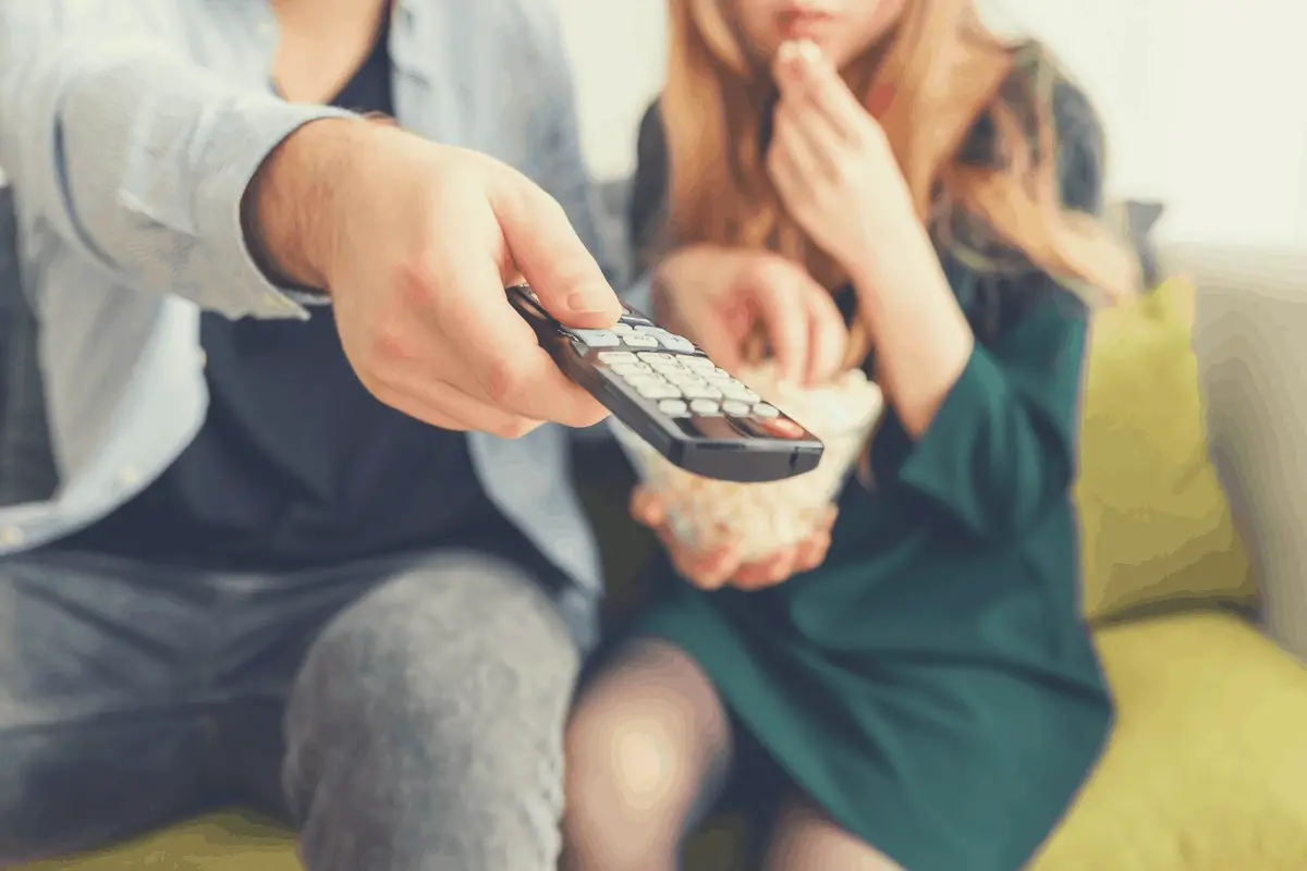 couple sitting in the couch with one turning on the TV