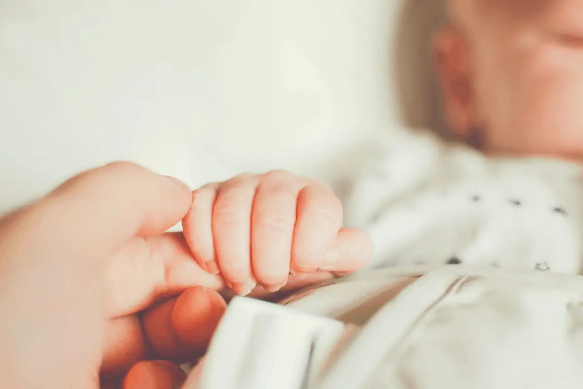 adult holding the hand of a sleeping baby