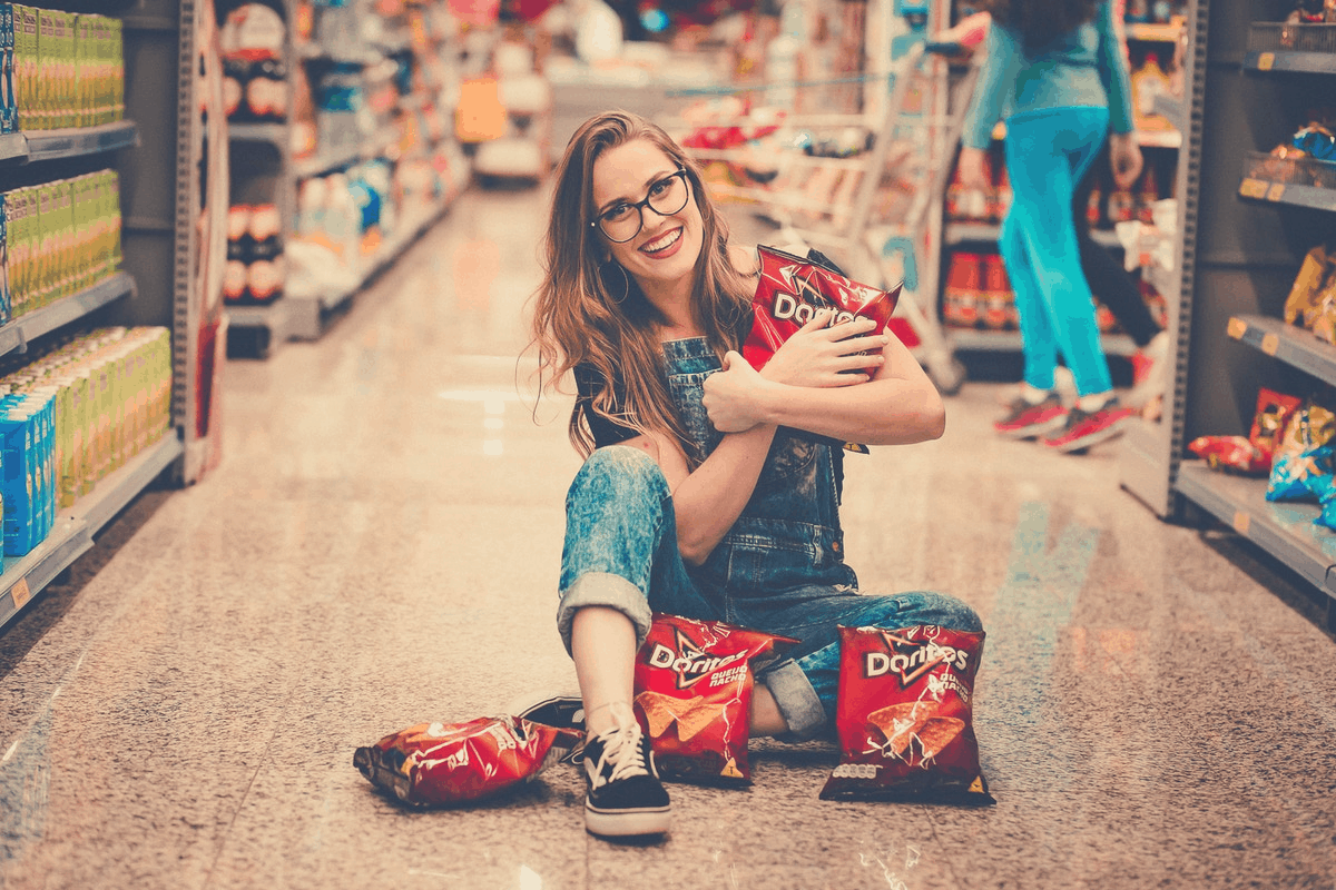 blonde woman sitting on a supermarket floor holding Doritos