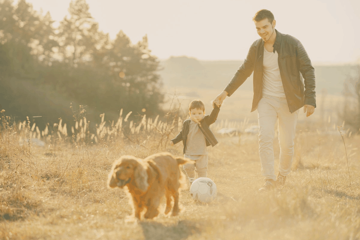 man and his son playing soccer outdoors with their dog