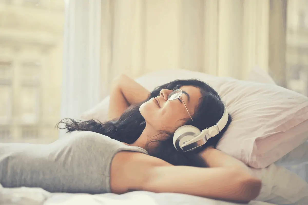 brunette in glasses listening to headphones in bed